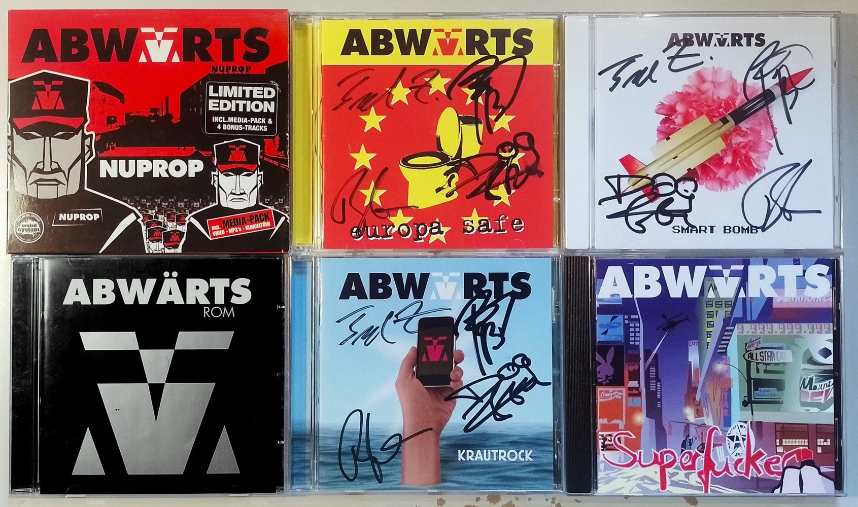 6 CDs by the band Abwärts laid out in a grid. The albums are from left to right: NuProp, Rom, Europa Safe, Krautrock, Smart Bomb and Superfucker. Europa Safe, Krautrock and Smart Bomb are signed